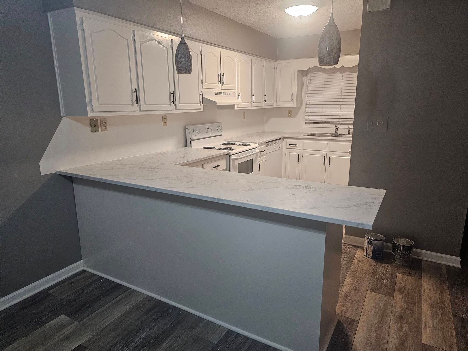 Narrow hallway with dark wood floors, white walls, and closed doors. A window is at the end of the hall.
