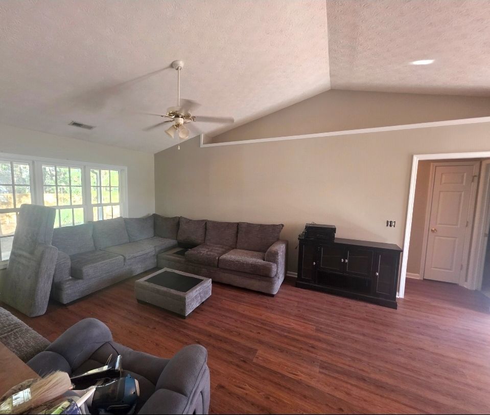 Narrow hallway with dark wood floors, white walls, and closed doors. A window is at the end of the hall.