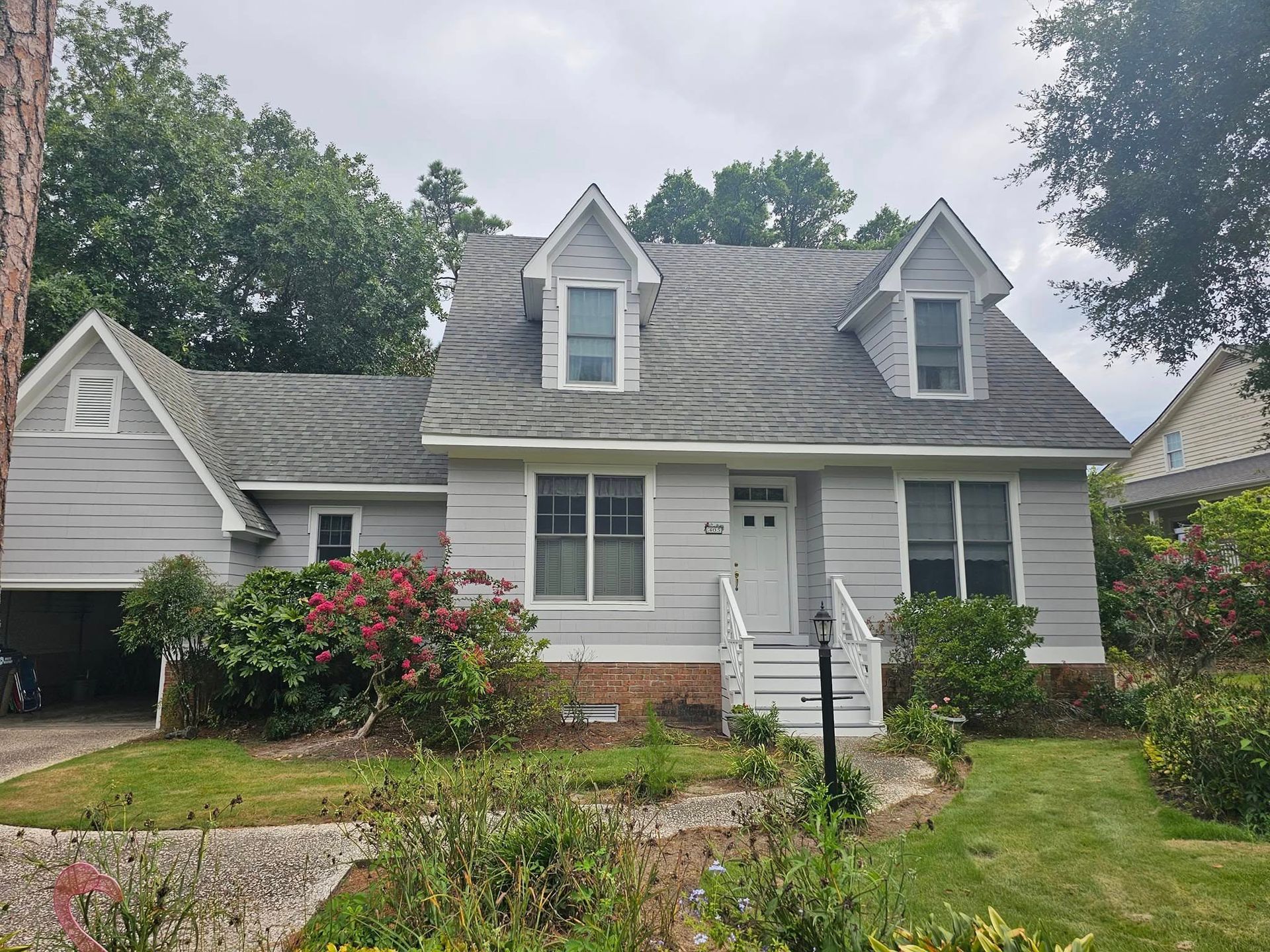 Gray house with a grey roof, dormers, and a small front garden under an overcast sky.