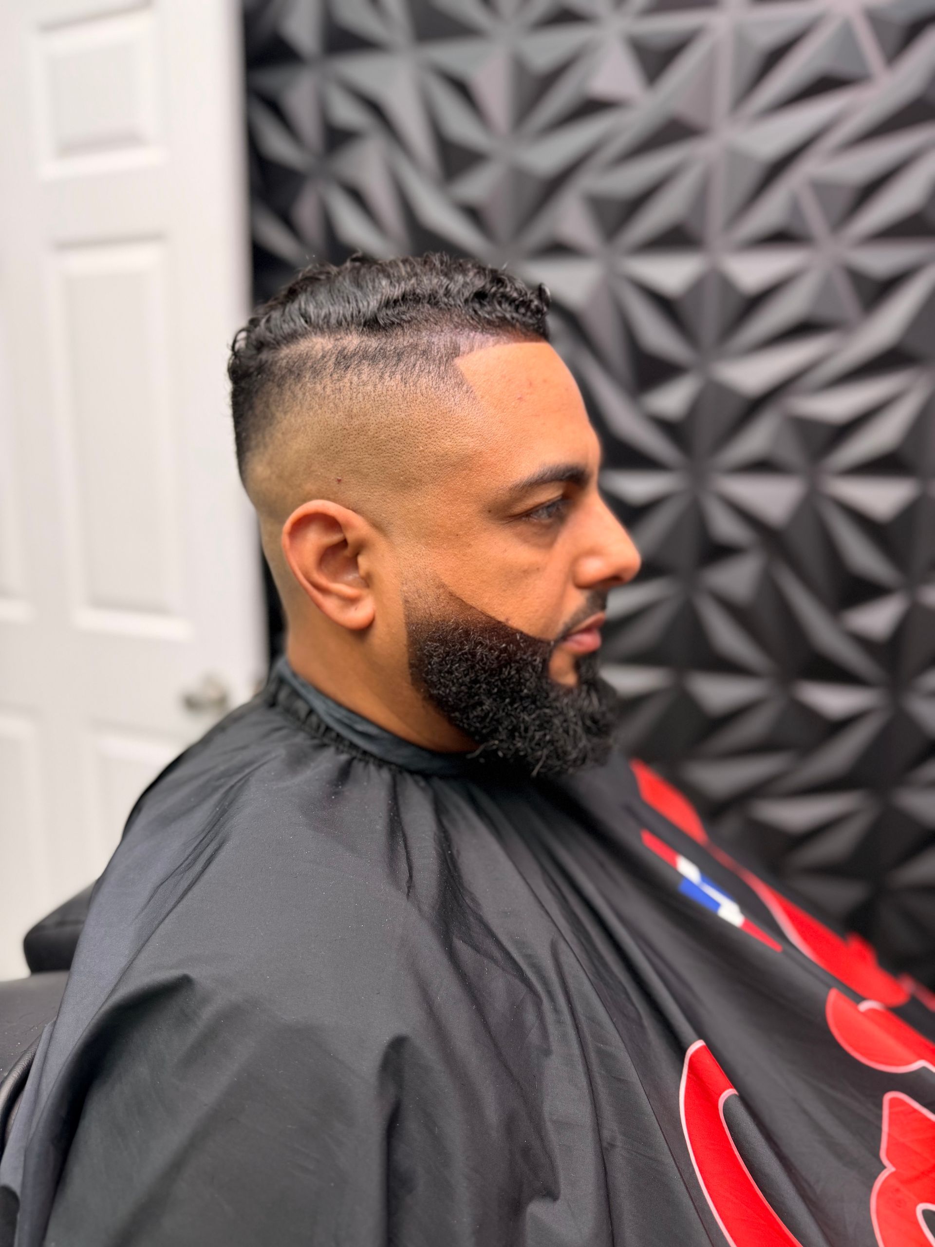 Side-profile haircut of a man in a black barber cape in a barbershop chair