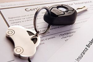 Car key and car-shaped keyring on top of car insurance paperwork.