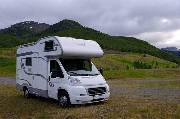 White RV parked in a grassy field, green hills and cloudy sky in the background.