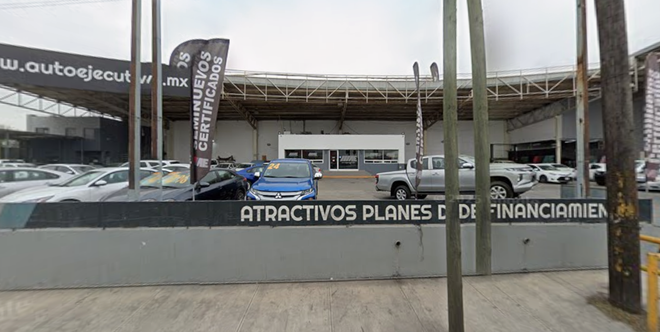 Car dealership exterior with parked cars, flags, and a sign reading “Atráctivos planes de financiación.”