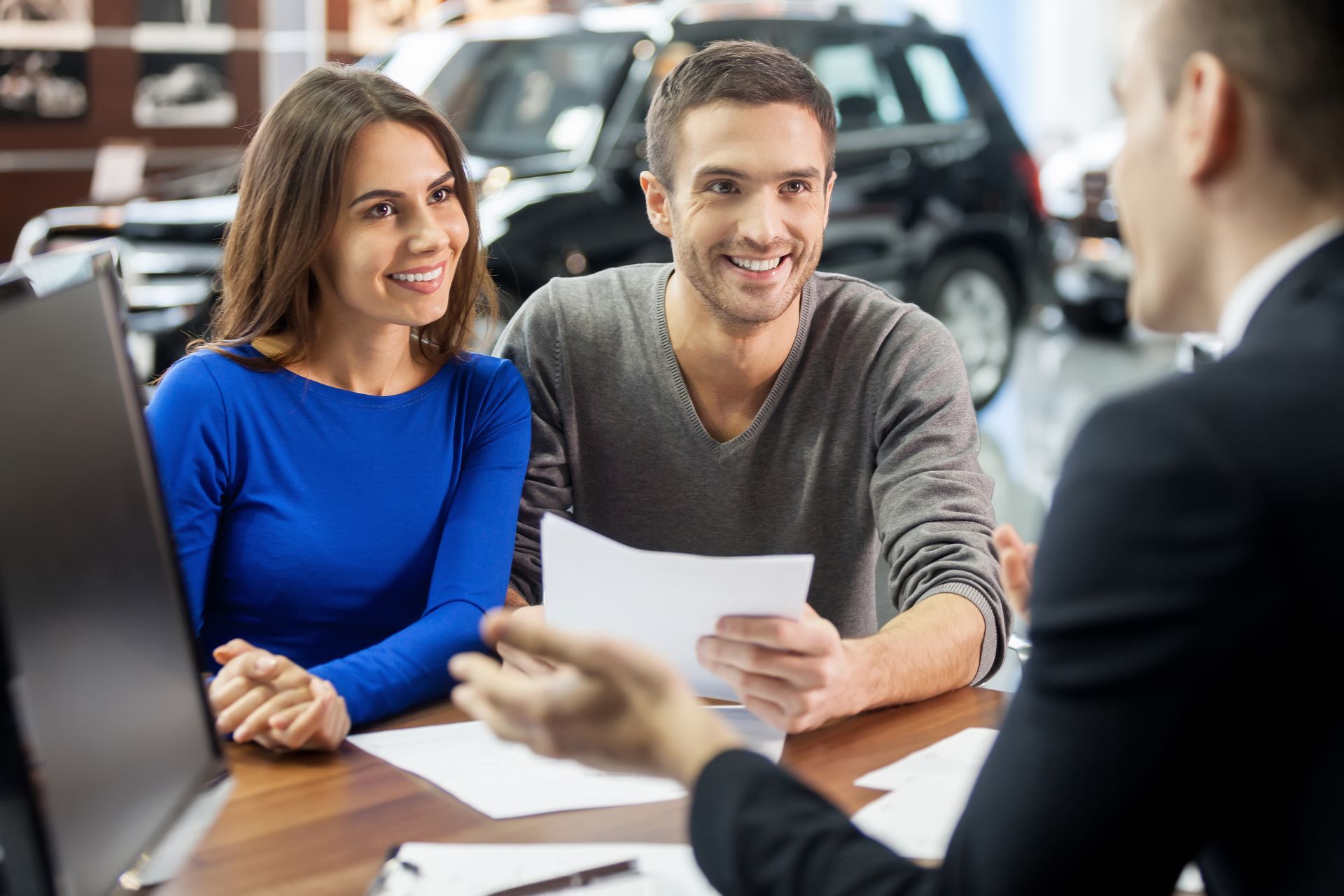 Una pareja se reúne con un vendedor de coches en un concesionario y, sentados a una mesa, hablan sobre la documentación.