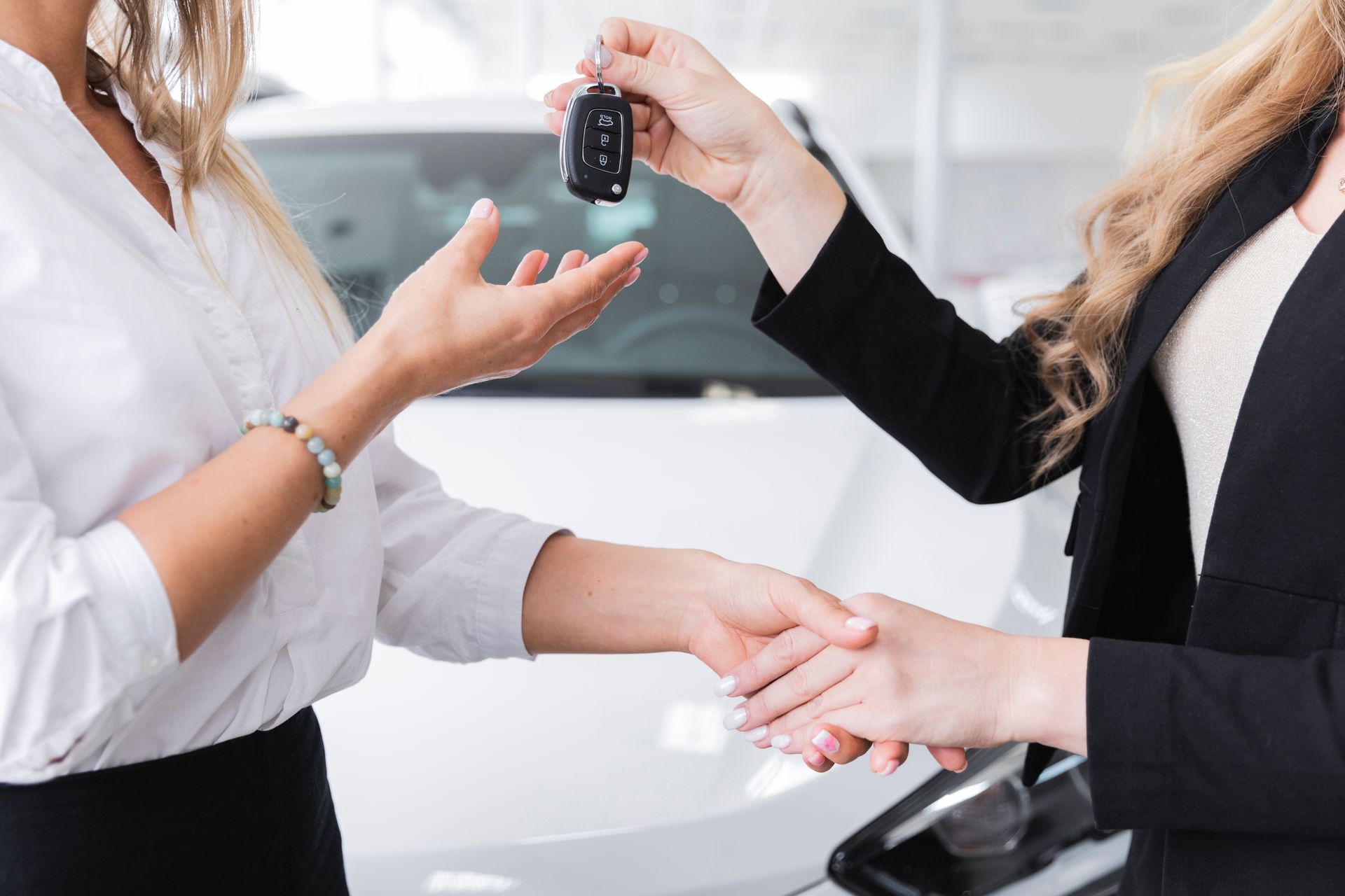Dos mujeres vestidas de negocios intercambiando llaves de coche en una sala de exposición de automóviles.
