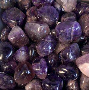 Pile of smooth, polished amethyst stones in various shades of purple.