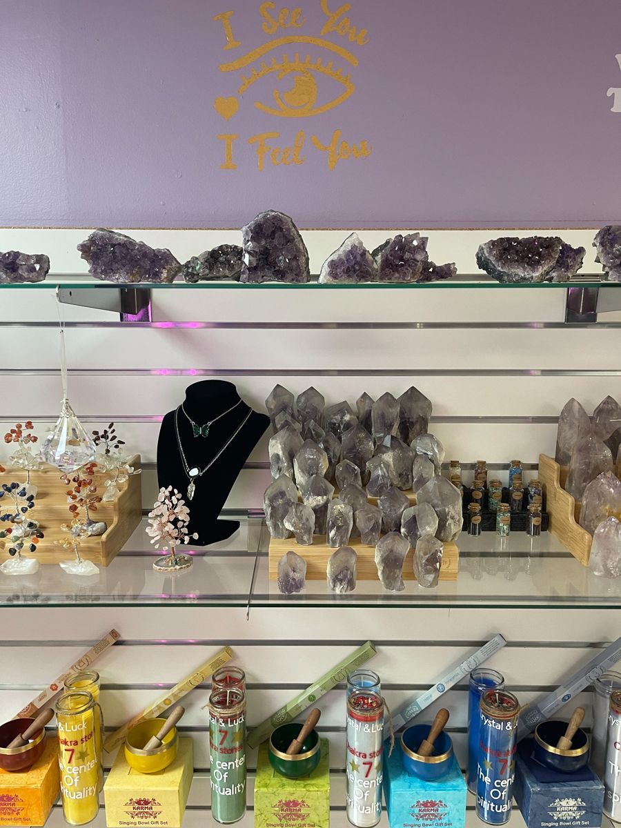 Shelves display crystals, candles, and jewelry in a shop with a purple wall and 