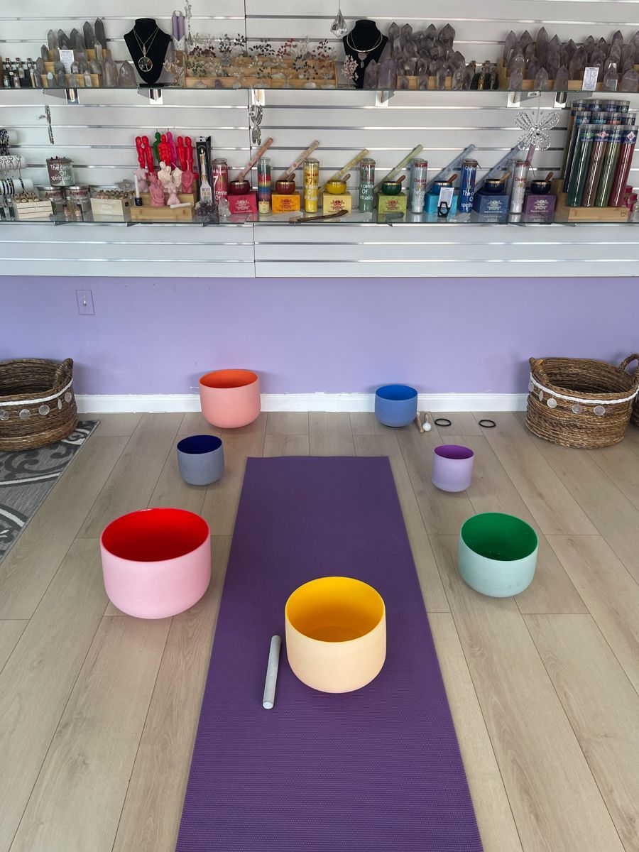 Room with yoga mat and colorful singing bowls, shelves with items in background.