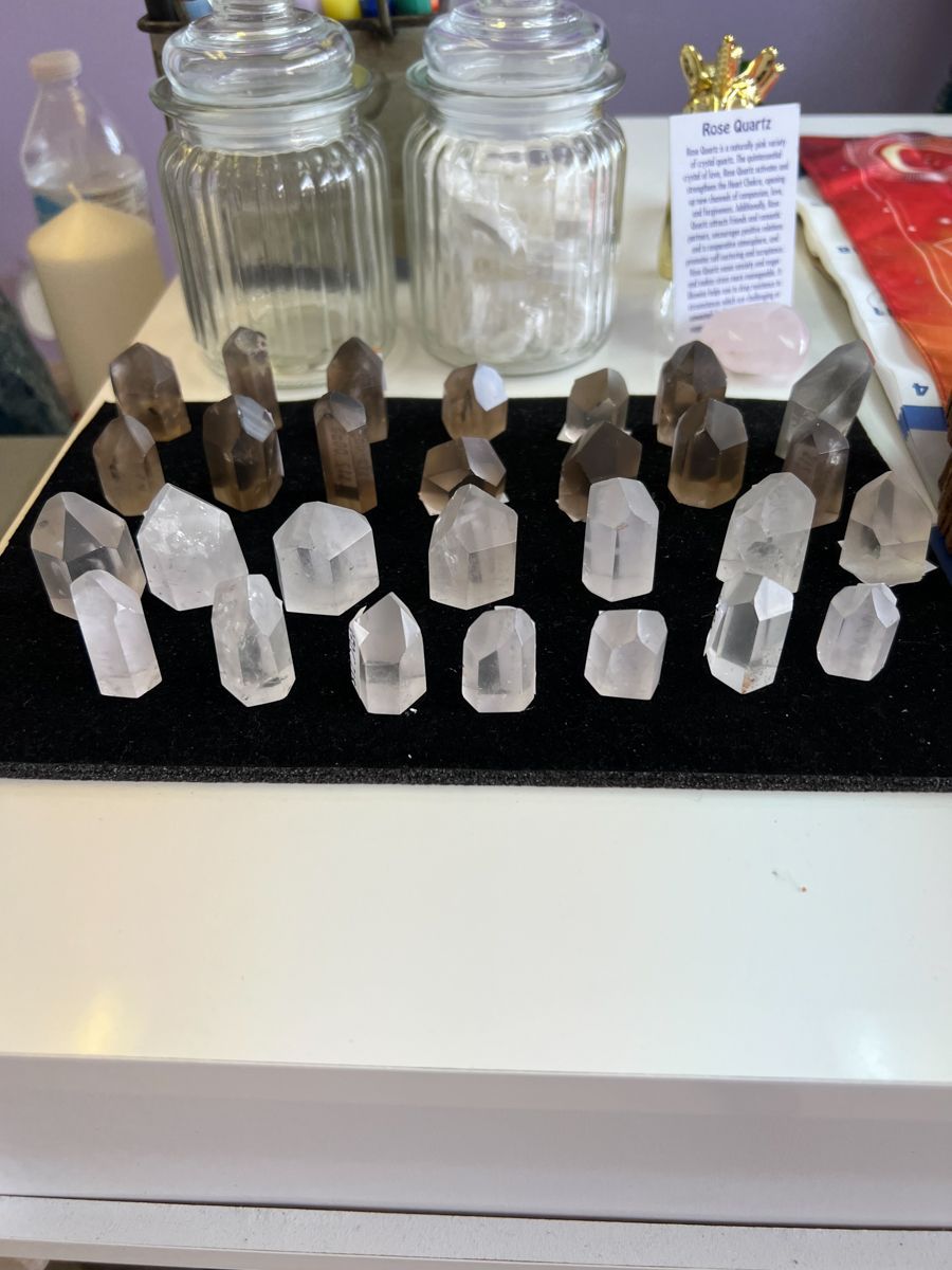 Rows of quartz crystals and jars on a white surface, with a sign in the background.