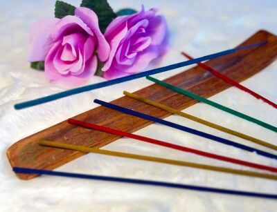 Incense sticks on a wooden holder with purple roses in the background.