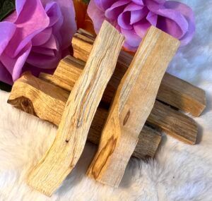 Palo Santo sticks, light-colored wood, with purple flowers on a fluffy white surface.