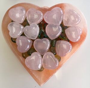 Pink heart-shaped gemstones in a heart-shaped dish with green and brown glass beads.