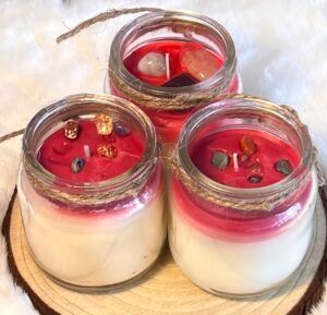 Three candles in glass jars, red wax with crystals, sitting on a wooden slab.
