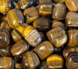 Tumbled tiger's eye gemstones, brown with golden bands, filling the frame.