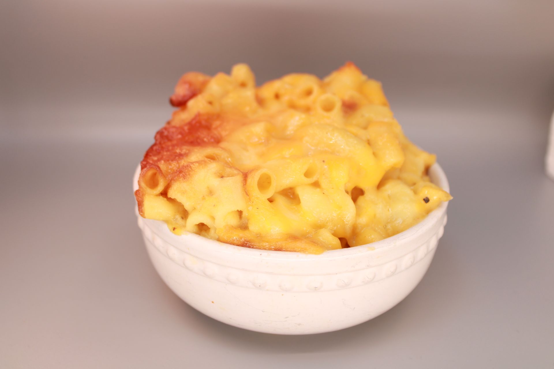 Mac and cheese in a white bowl, baked with a golden-brown top.