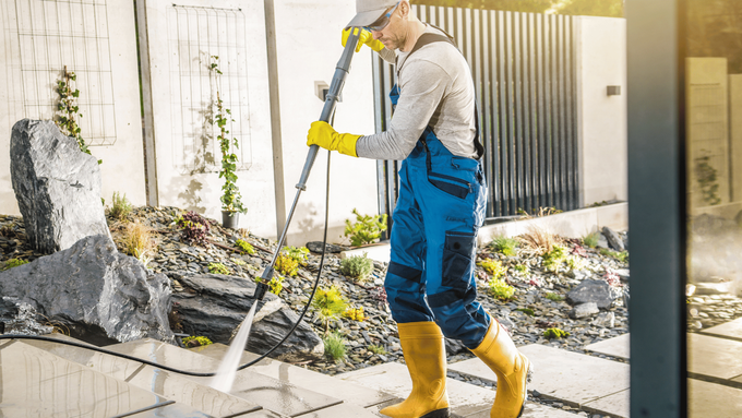 A man is cleaning a sidewalk with a high pressure washer.