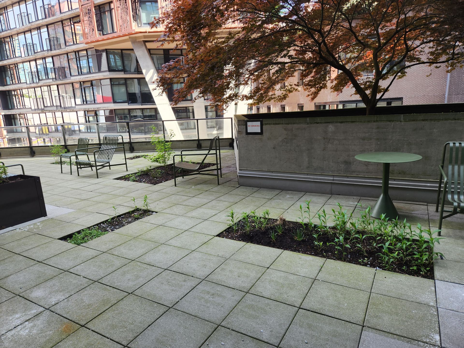 Rooftop patio with stone pavers, small plants, metal furniture, and a building in the background.