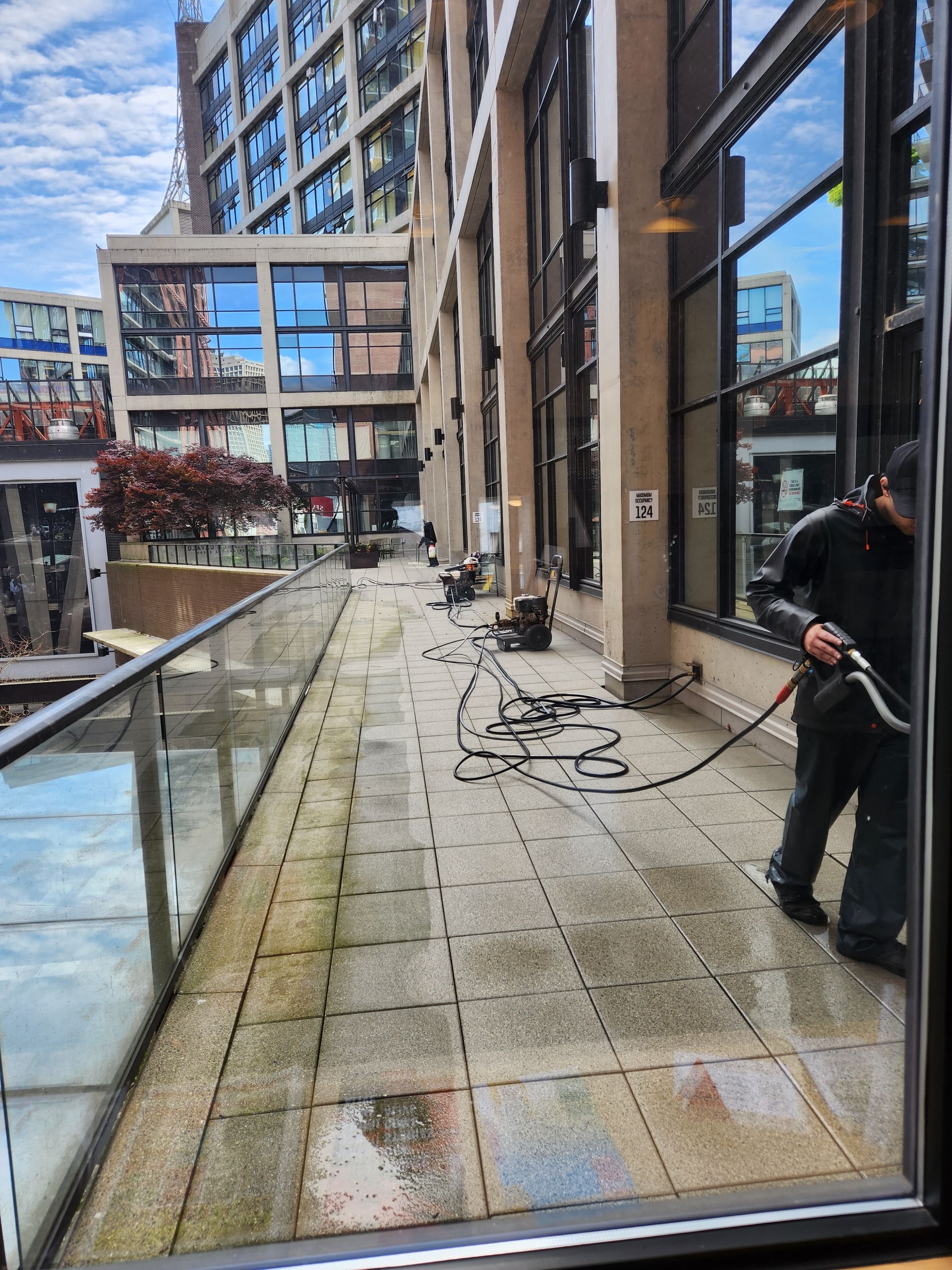 A person cleaning a patio with power washer. Buildings in background.