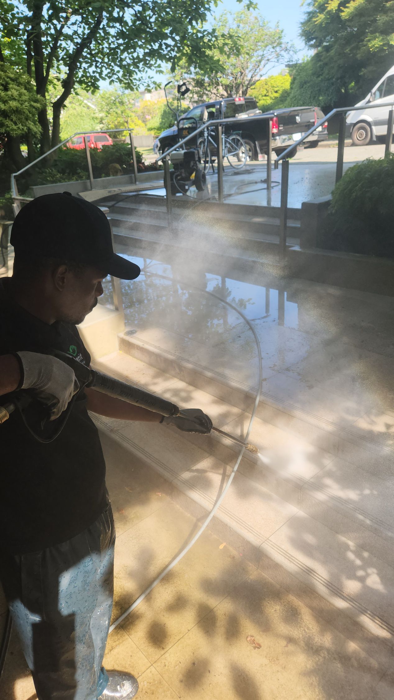 Man power washing a concrete surface outdoors with a hose; light colored ground reflecting the sun.