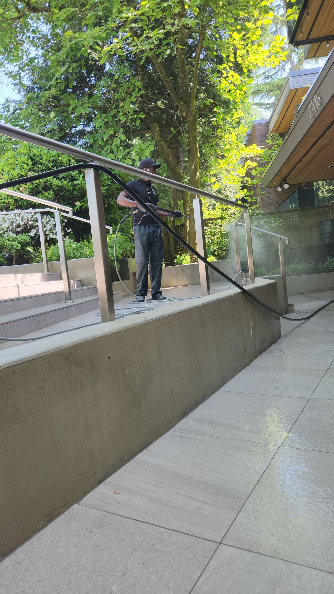 Man power washes a patio with a hose. Sunlight illuminates the scene.