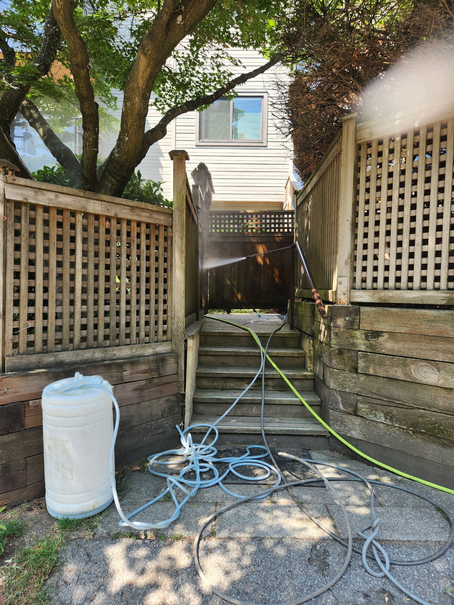 Person pressure washing wooden stairs and fence in an outdoor setting. Water spray visible.