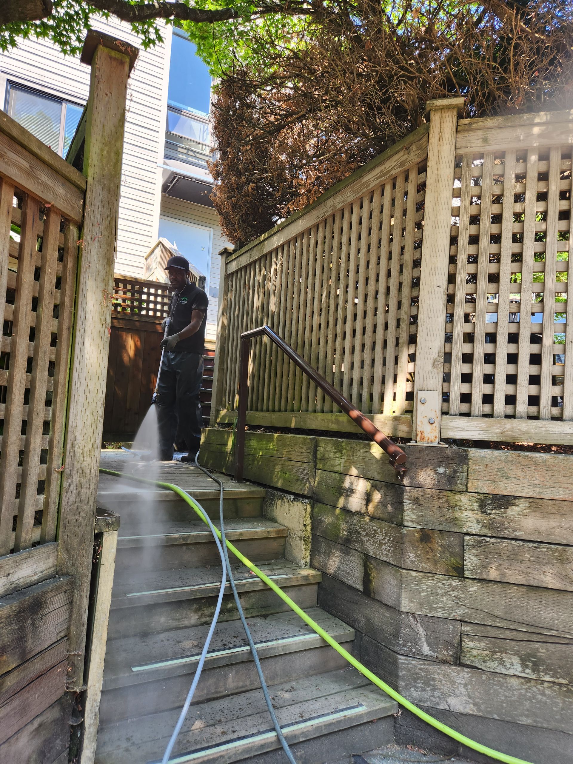 Person power washing outdoor stairs and wooden fence.