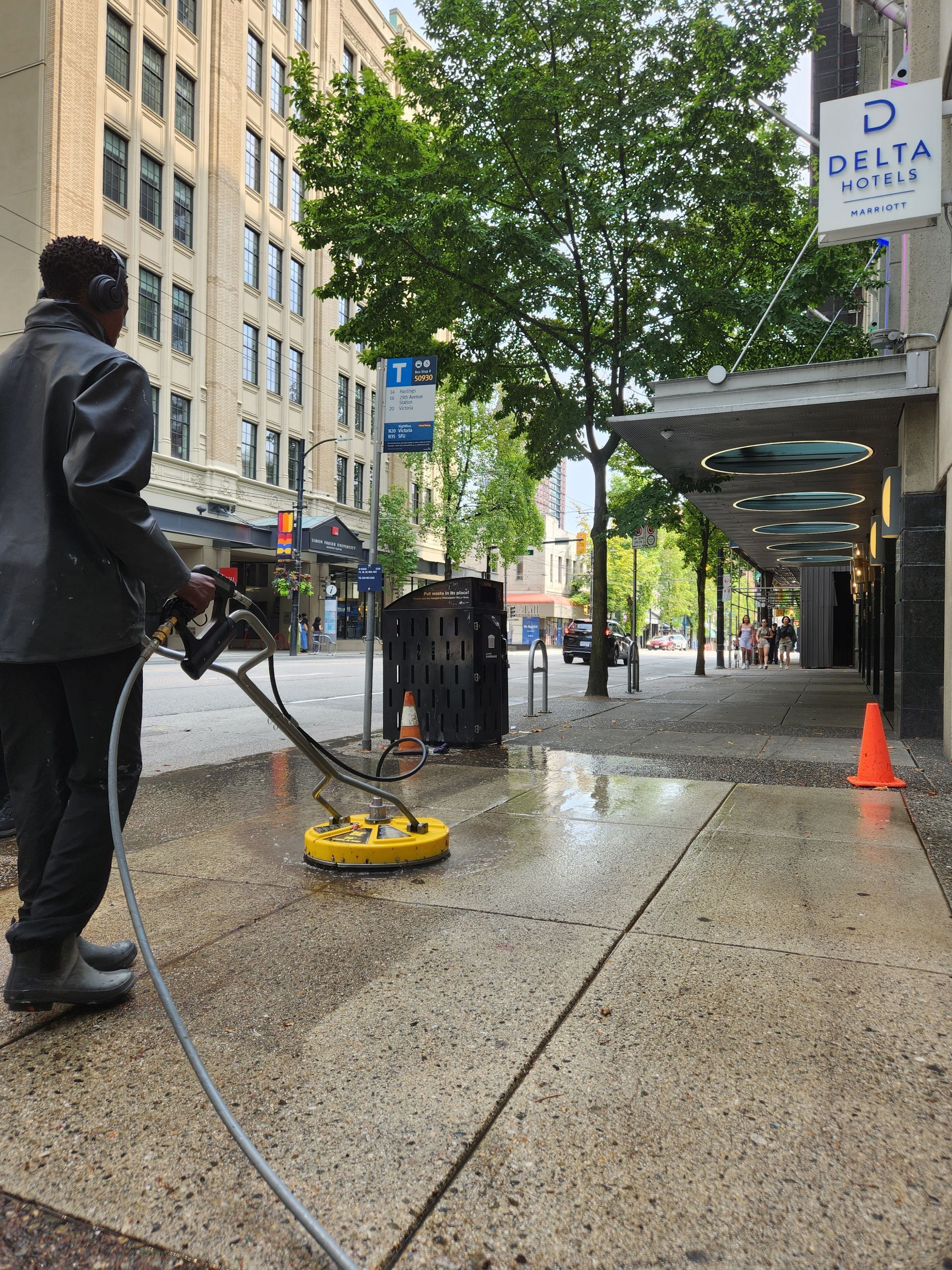 A person uses a yellow power washer on a city sidewalk in front of a Delta Dental building.