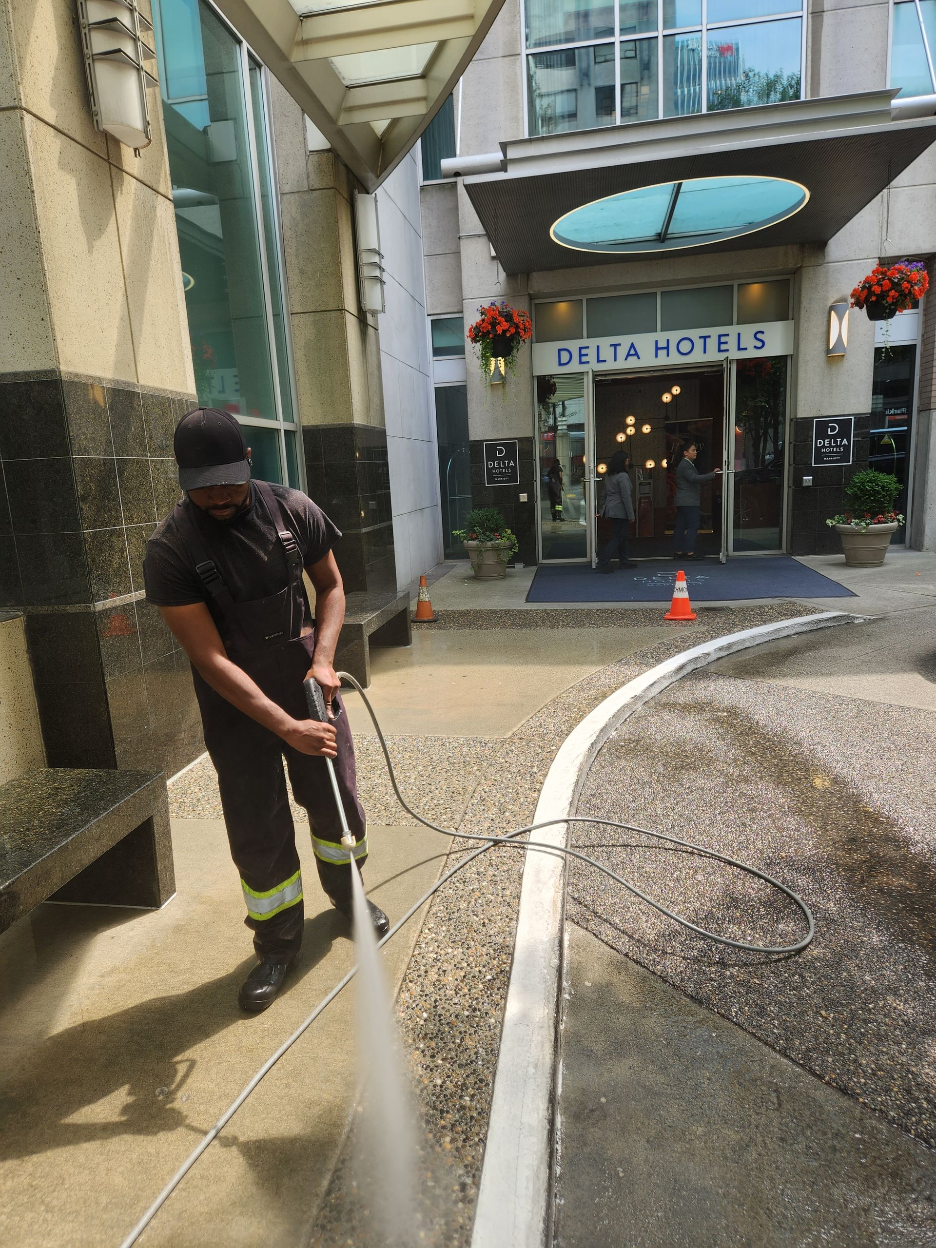 A worker uses a power washer to clean a paved walkway in front of a Delta Hotels entrance.