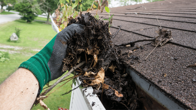 A person is cleaning a gutter from a roof.