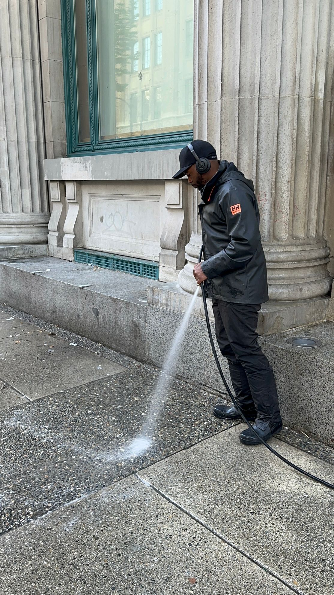 A man is cleaning the sidewalk with a pressure washer.