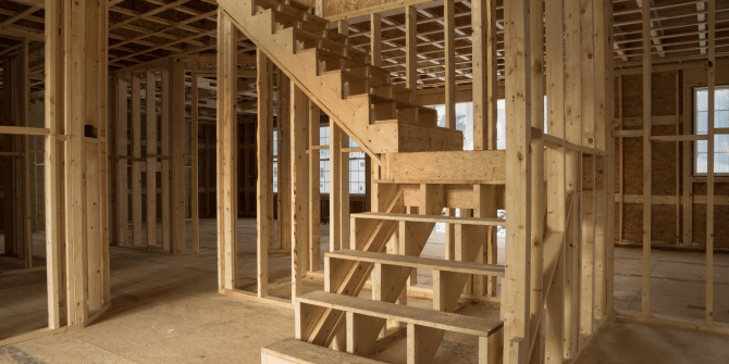 A wooden staircase is being built in a house under construction.