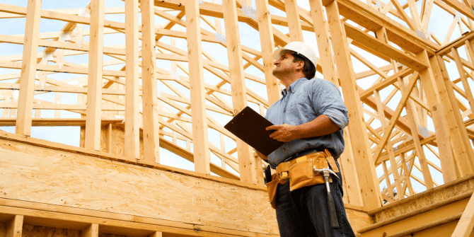 A man is standing in front of a wooden structure holding a clipboard.