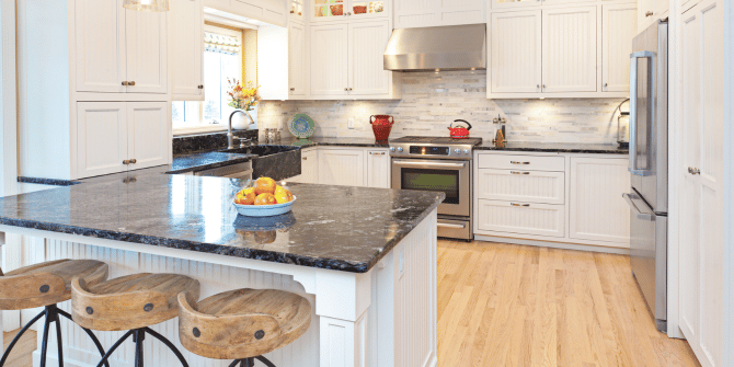 A kitchen with white cabinets , stainless steel appliances , granite counter tops and wooden floors.