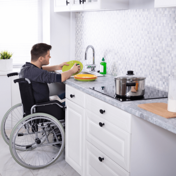 A man in a wheelchair washing dishes in a kitchen