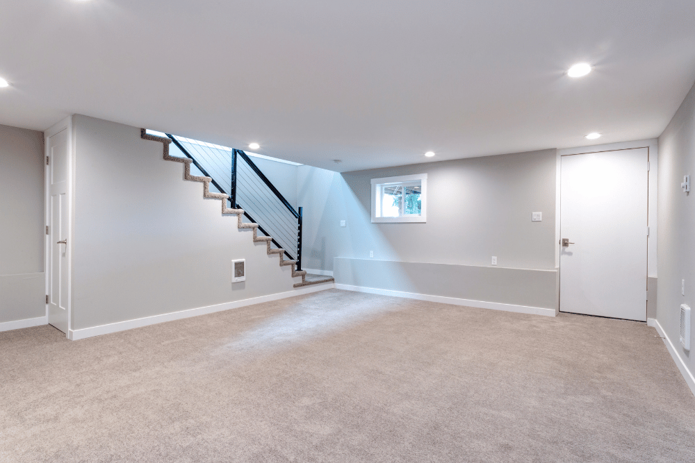 An empty basement with a staircase and a window.