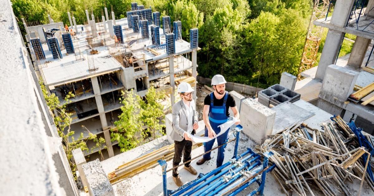 Two construction workers are standing on top of a scaffolding at a construction site.