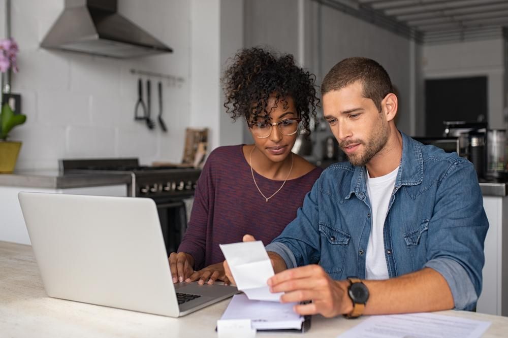 A man and a woman are sitting at a table looking at a laptop.