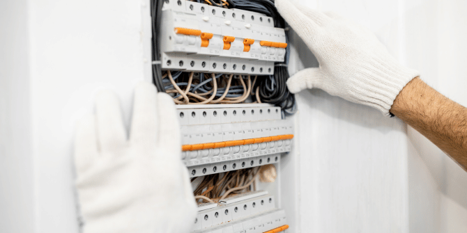 A man wearing white gloves is working on an electrical box.