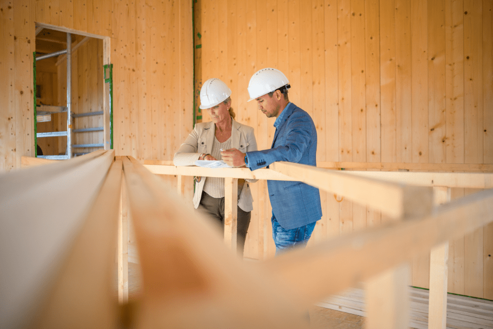 A man and a woman are looking at a blueprint at a construction site.