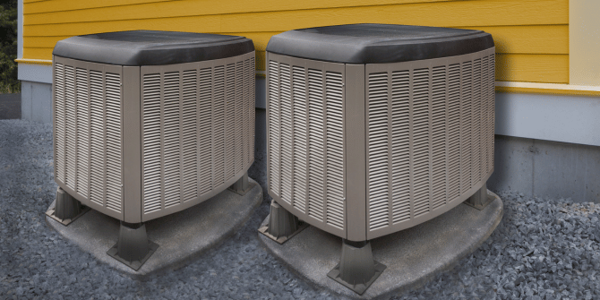 Two air conditioners are sitting next to each other on the side of a house.