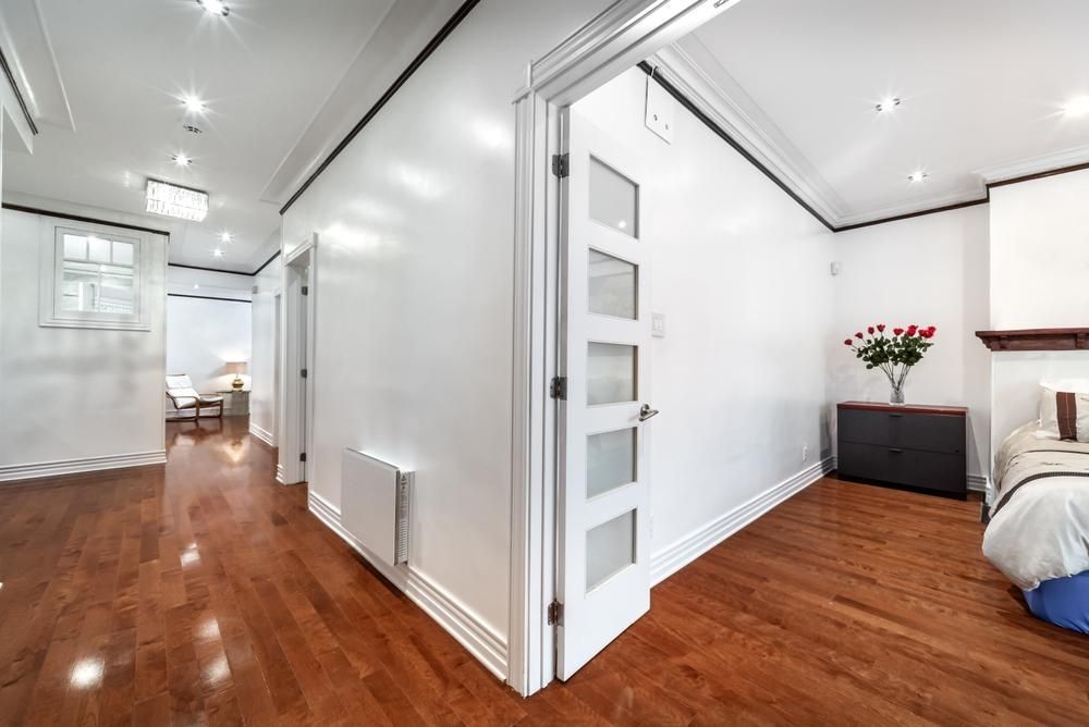 A hallway with hardwood floors and white walls leading to a bedroom.