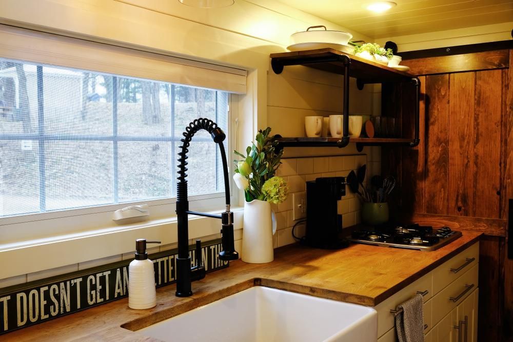 This kitchen has a rustic and vintage feel, with natural wood finishes and traditional details. The cabinets are made of wood and have a natural, unfinished look, giving the kitchen a warm and organic feel. The cabinet doors have a simple panel design, which is a classic and timeless style. The countertops are made of butcher block wood, which is a durable and practical choice for a kitchen workspace. The backsplash is made of white subway tiles, which is a classic and versatile option that complements the vintage style of the kitchen. The kitchen features a vintage-style gas range with a stainless steel finish, which adds a touch of modernity to the space. The sink is a traditional porcelain farmhouse sink, which is a classic choice for a vintage-style kitchen. The kitchen island is made of natural wood and features a butcher block countertop, which offers additional workspace and storage.