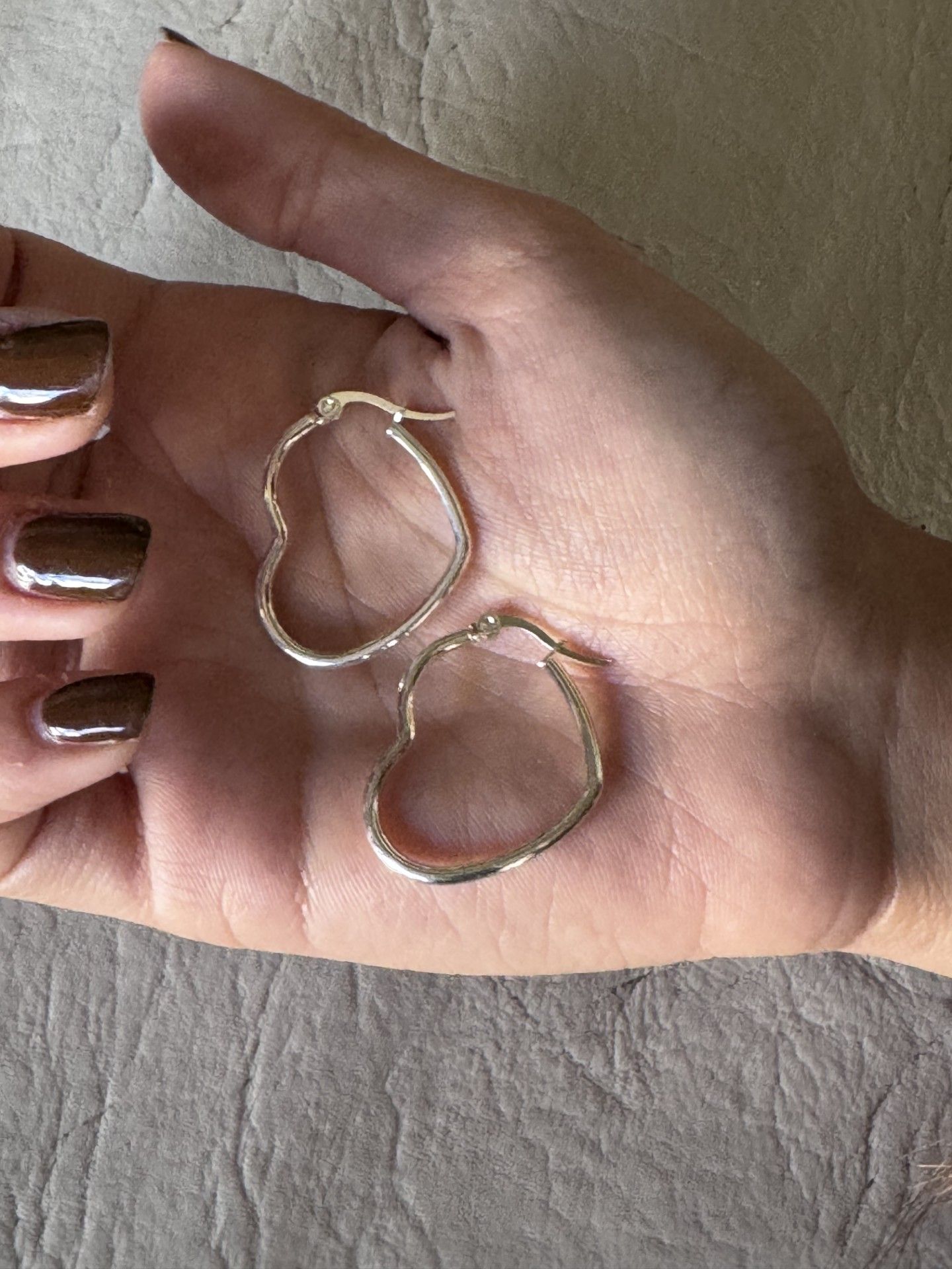 Una persona sostiene un par de pendientes de aro en forma de corazón en su mano.
