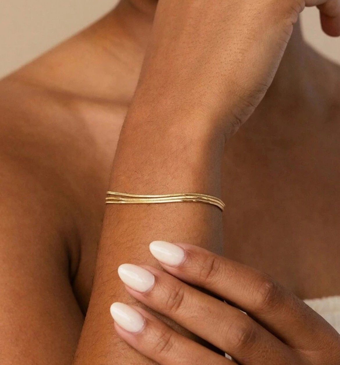 Muñeca de persona con pulsera de oro, mano con uñas blancas pulidas.
