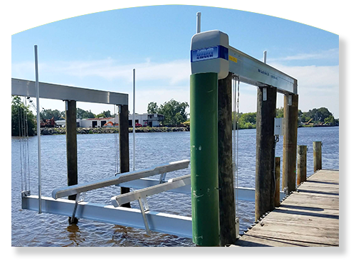 Boat lift over water, with a dock on the right. Blue sky, green and brown posts.