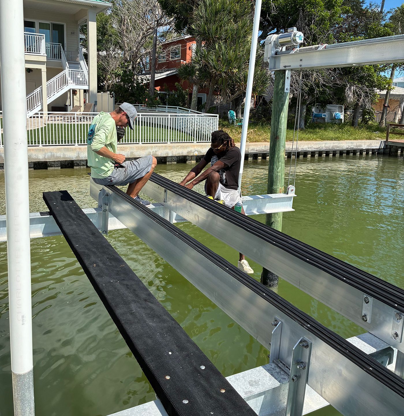 Two people working on a boat lift in a canal. One is seated, the other is kneeling.