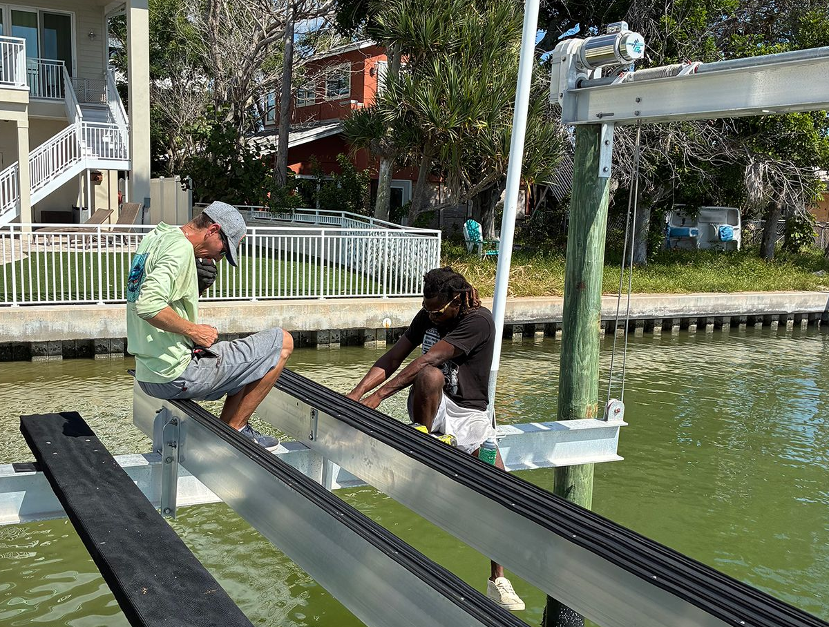 Two people installing a boat lift at a waterfront location.