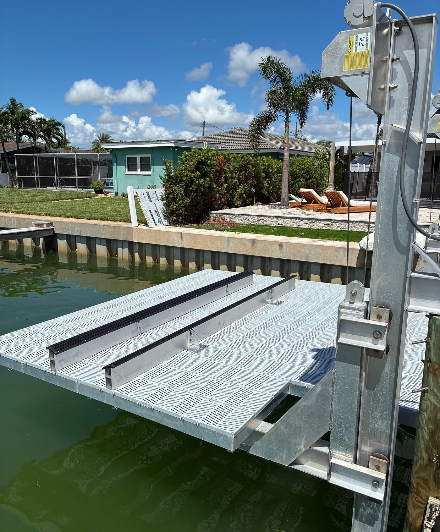 Boat lift platform extending over water with residential homes in background.