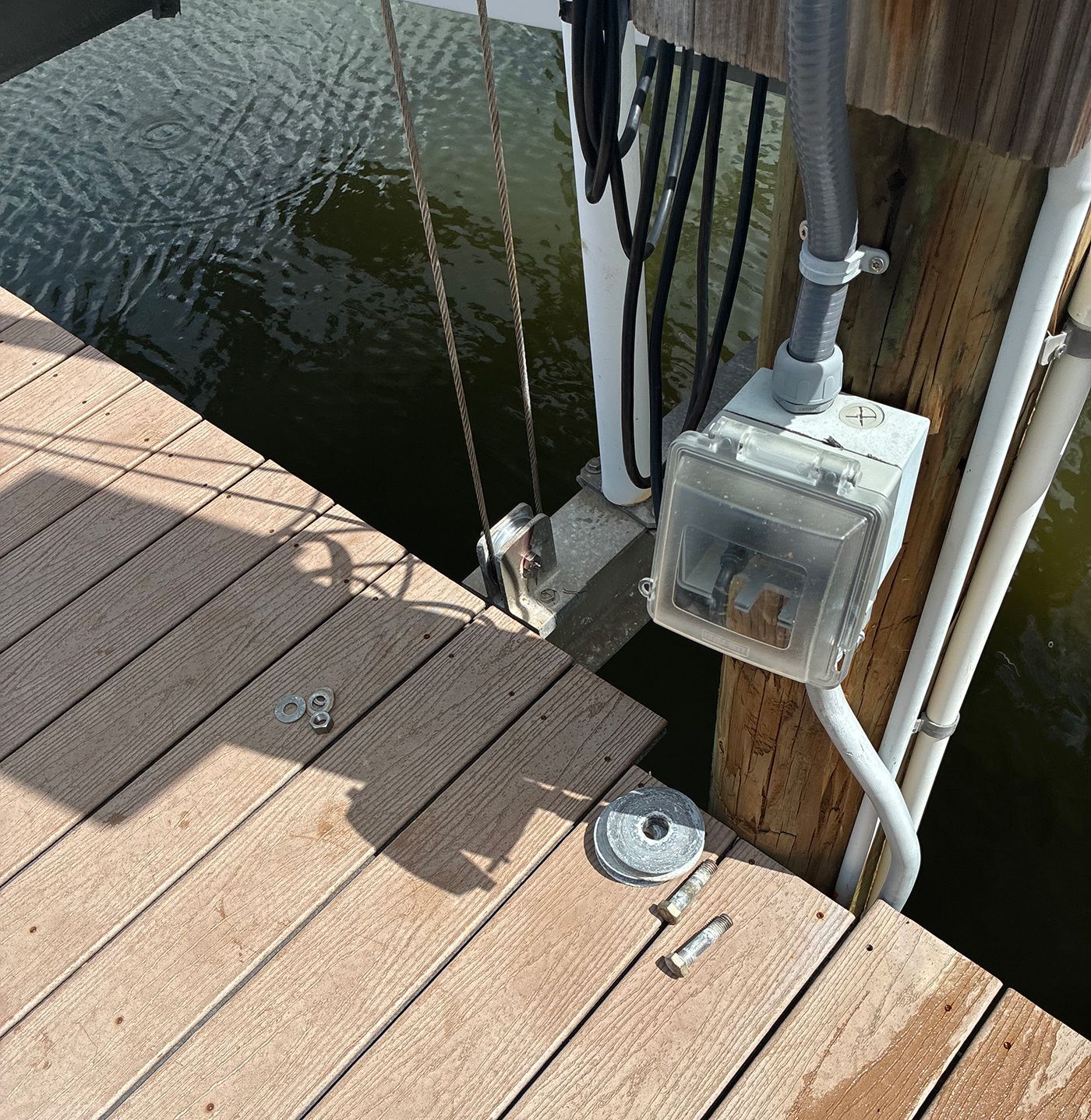 Dockside electrical box and cables on a wooden dock next to water.