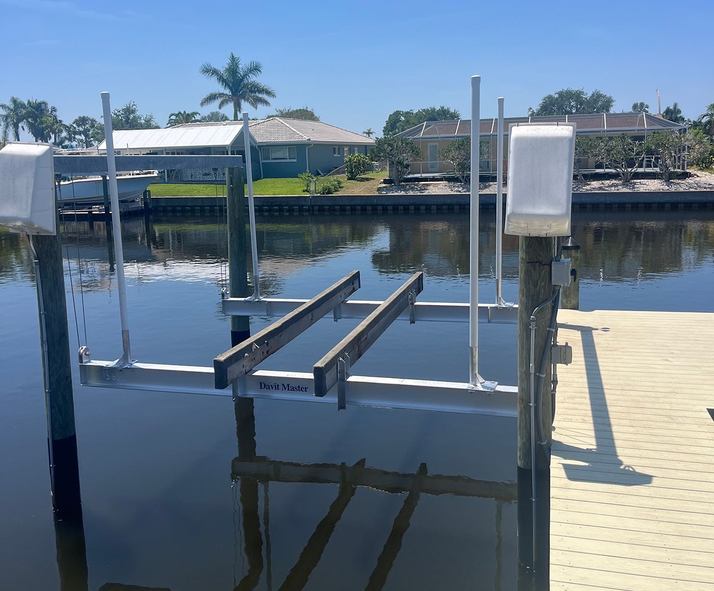 Boat lift in a canal with a dock, set against a backdrop of waterfront homes under a sunny sky.